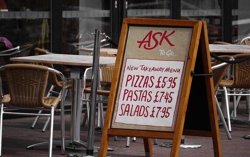A Board Sign outside cafe seating area advertising Pizza prices