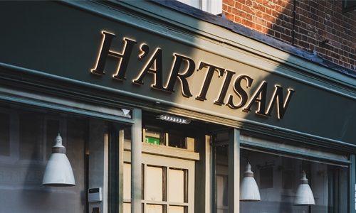 H'artisan Coffee Shop Signage With Black 3D built up letters against a forest green sign fascia and warm white led halo illumination