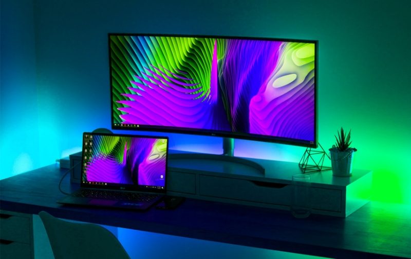 Desk with laptop connected to monitor, with blue and green LED illumination behind the monitor