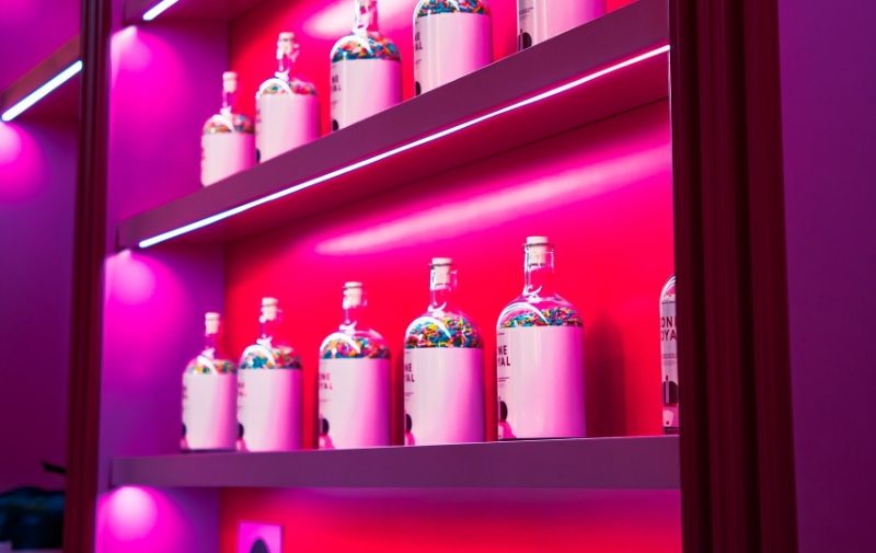 Shelves containing bottles illuminated by pink coloured led strip lights on each shelf