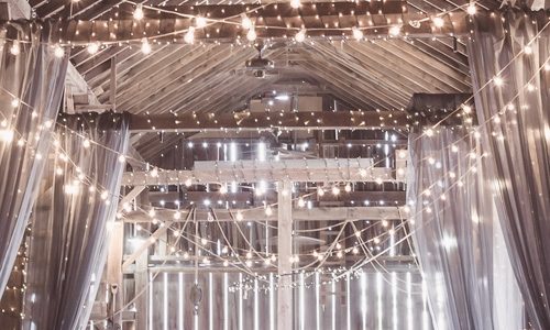 Wedding lighting in a barn with festoon string lights and fairy lights draped over white curtains